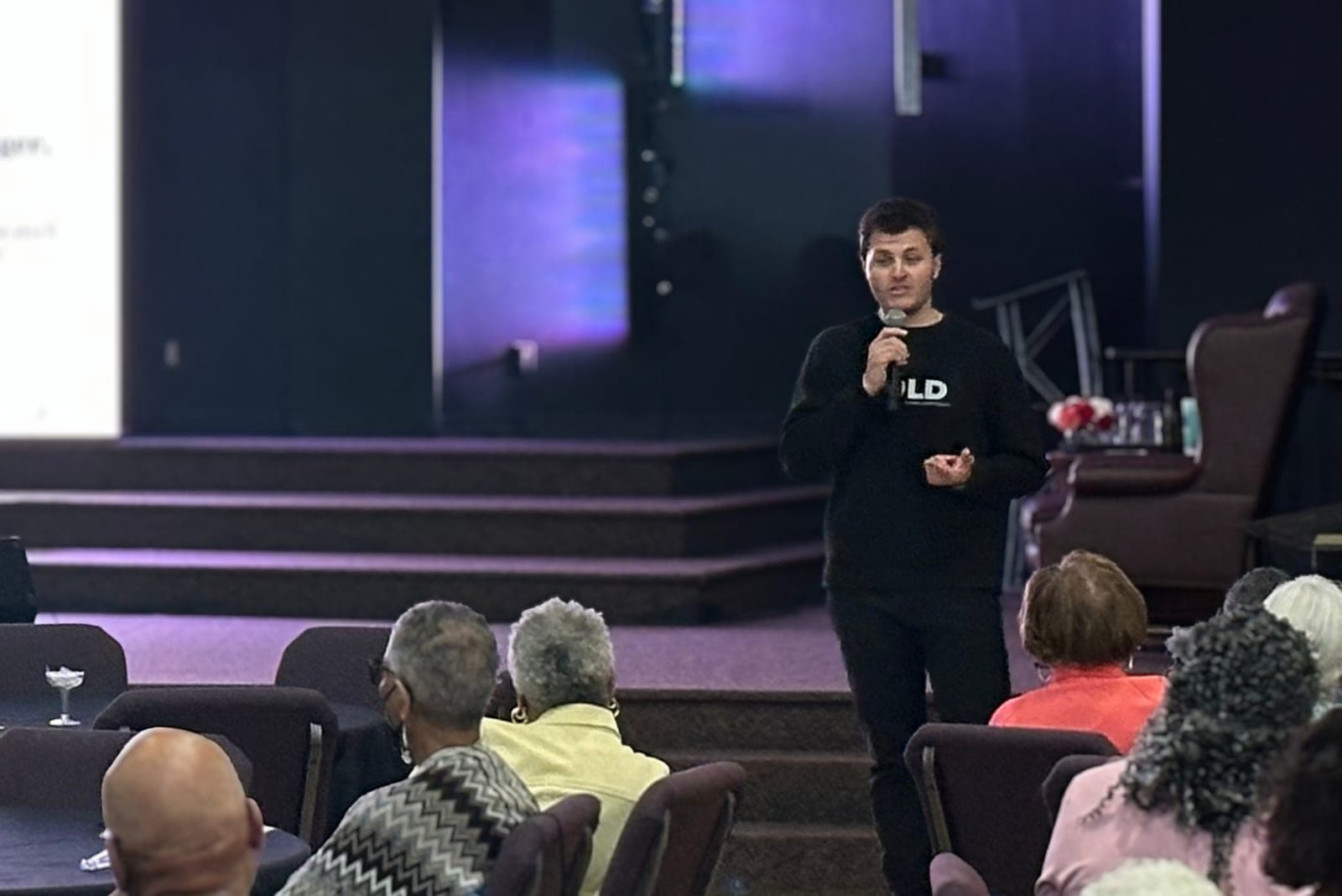 A GOLD presenter speaking to a seated audience in a church sanctuary