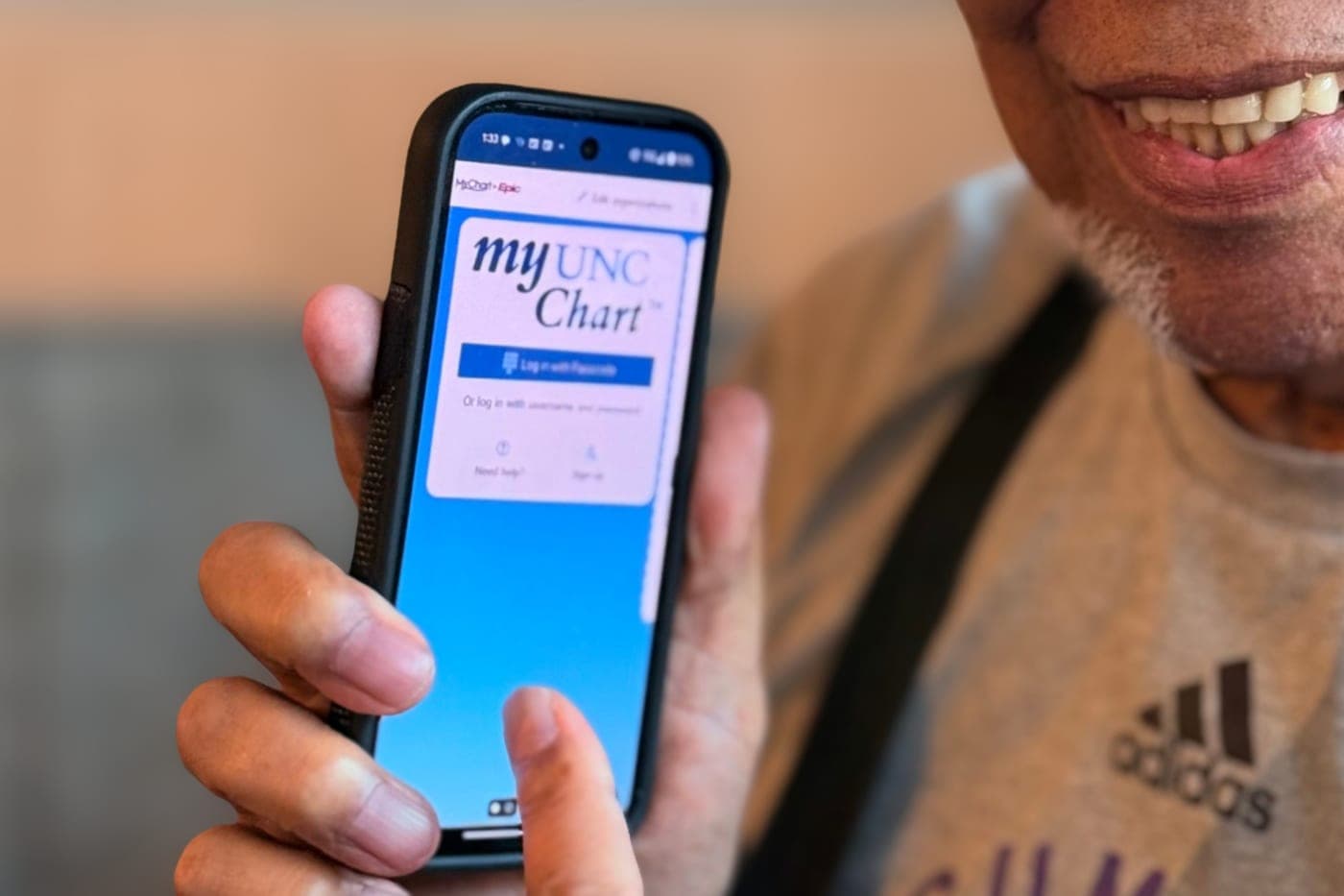 A GOLD member holding his phone, open to the myUNC Chart login screen