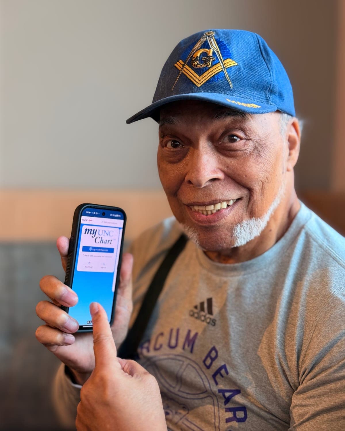 A GOLD member smiling as he shows his phone, open to the myUNC Chart login screen