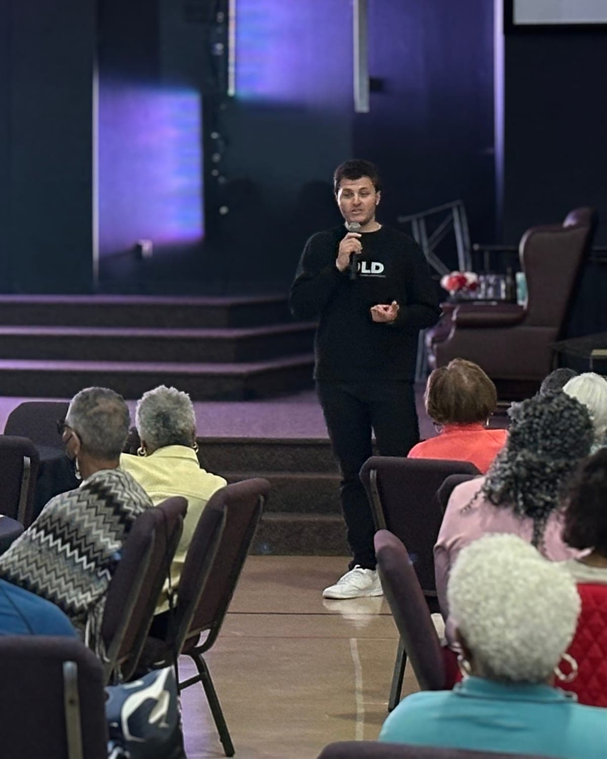 A GOLD presenter speaking from the stage to a seated audience