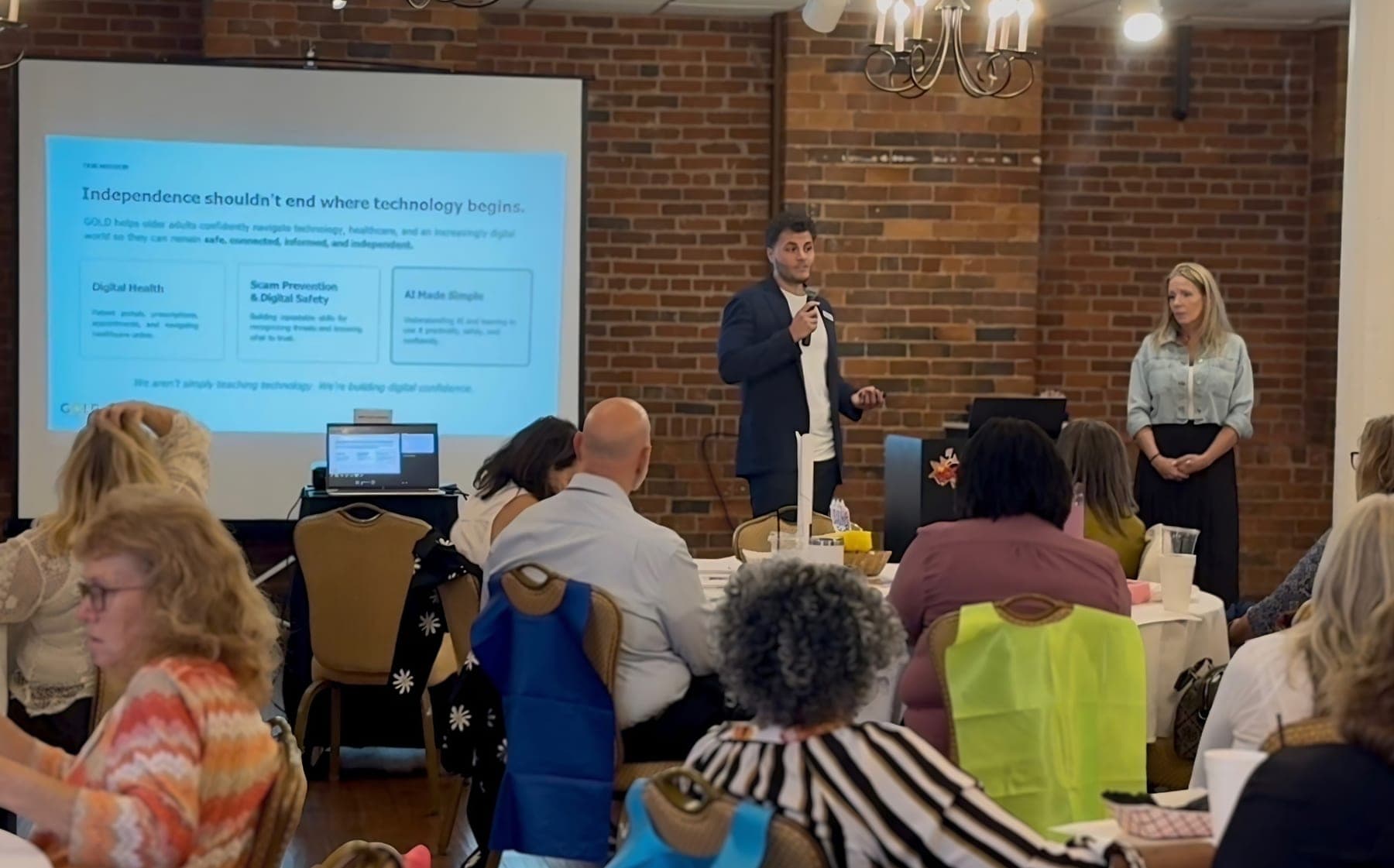 Two GOLD presenters leading a workshop for a seated room at a brick-walled venue